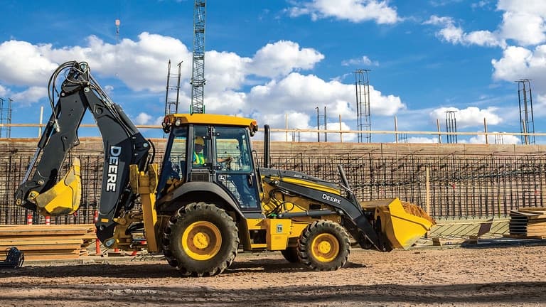 A 410P Backhoe with building materials and cranes in the background. | 4re Equipment
