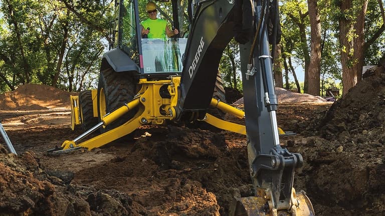 An operator using a 710P-Tier Backhoe to scoop dirt out of a hole. | 4re Equipment