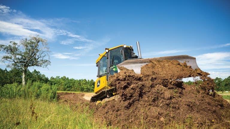 Front view of a 450P Dozer pushing dirt with trees in the background. | 4re Equipment