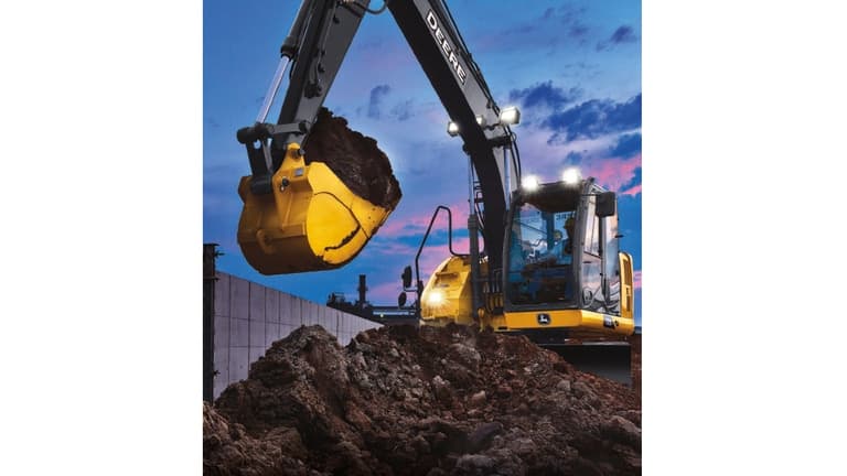A 135P-Tier Excavator with headlights scooping dirt from a pile at a worksite with sunset in the background. | 4re Equipment
