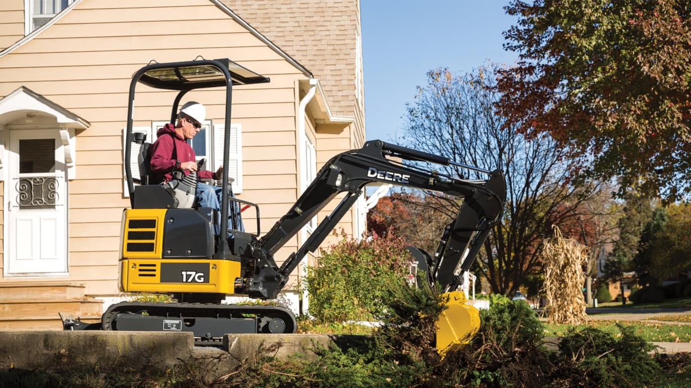 Man using 17G excavator to dig up a bush in front of a house. | 4re Equipment | ID: 017gxff