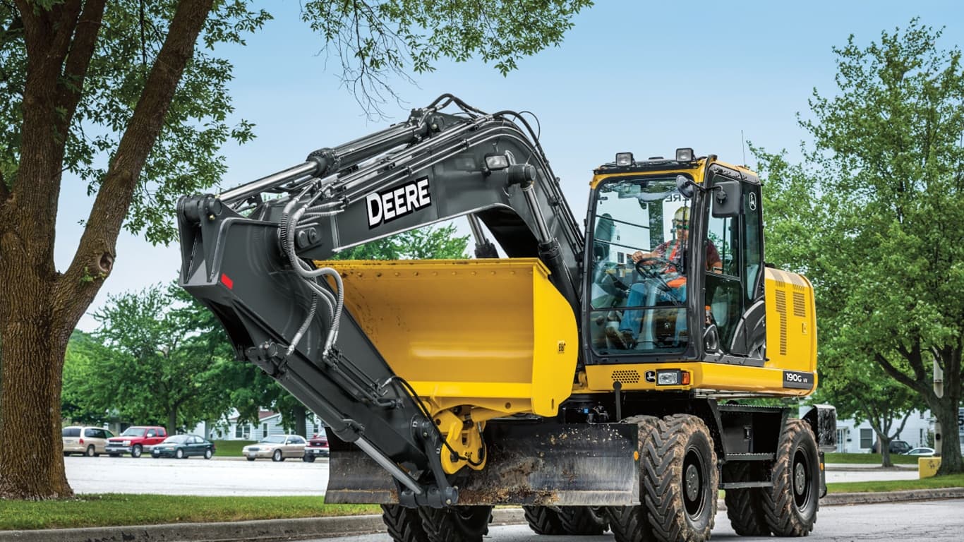 An operator driving a 190GW Excavator down a road with a parking lot in the background. | 4re Equipment | ID: 190gwff