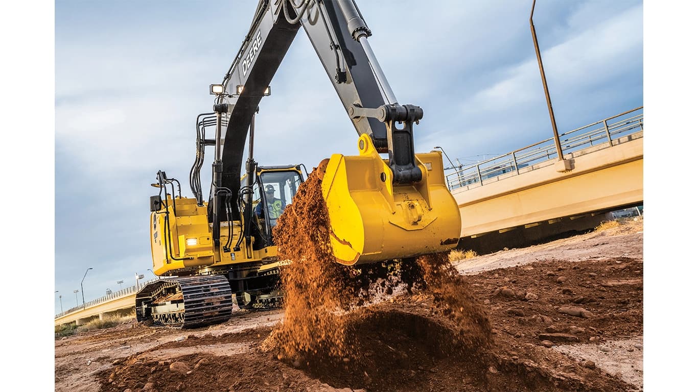 An operator using a 245 P-Tier Excavator to scoop dirt at a worksite with an overpass bridge in the background. | 4re Equipment | ID: 245PEXFT4