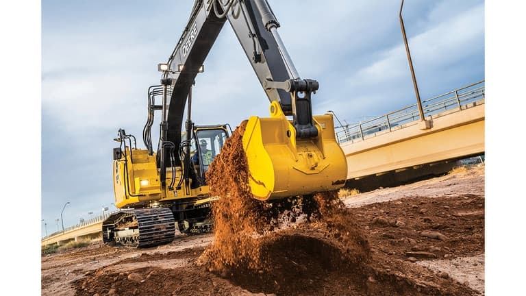 An operator using a 245 P-Tier Excavator to scoop dirt at a worksite with an overpass bridge in the background. | 4re Equipment