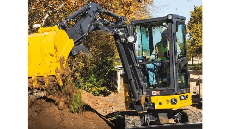 An operator using a 26P-Tier Excavator to dump dirt onto a pile in front of a fence. | 4re Equipment