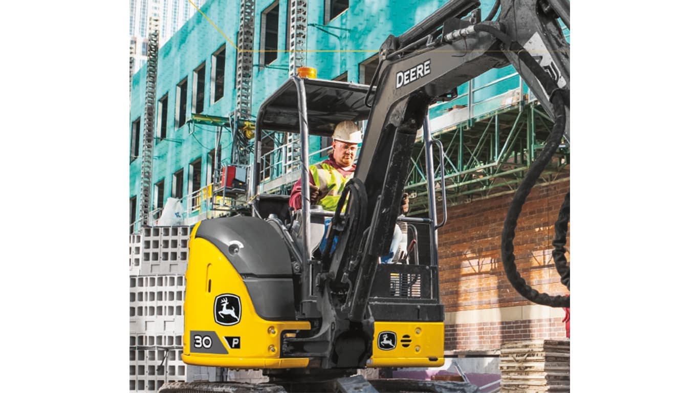 A close-up of an operator using a 30P-Tier Excavator at a worksite with buildings under construction in the background. | 4re Equipment | ID: 30PEXFT4