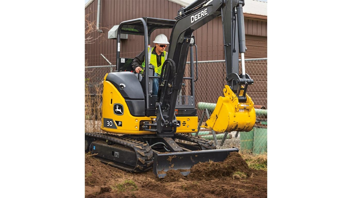 An operator using a 30P-Tier Excavator to move dirt at a worksite with a fence and brown building in the background. | 4re Equipment | ID: 30PEXFT4