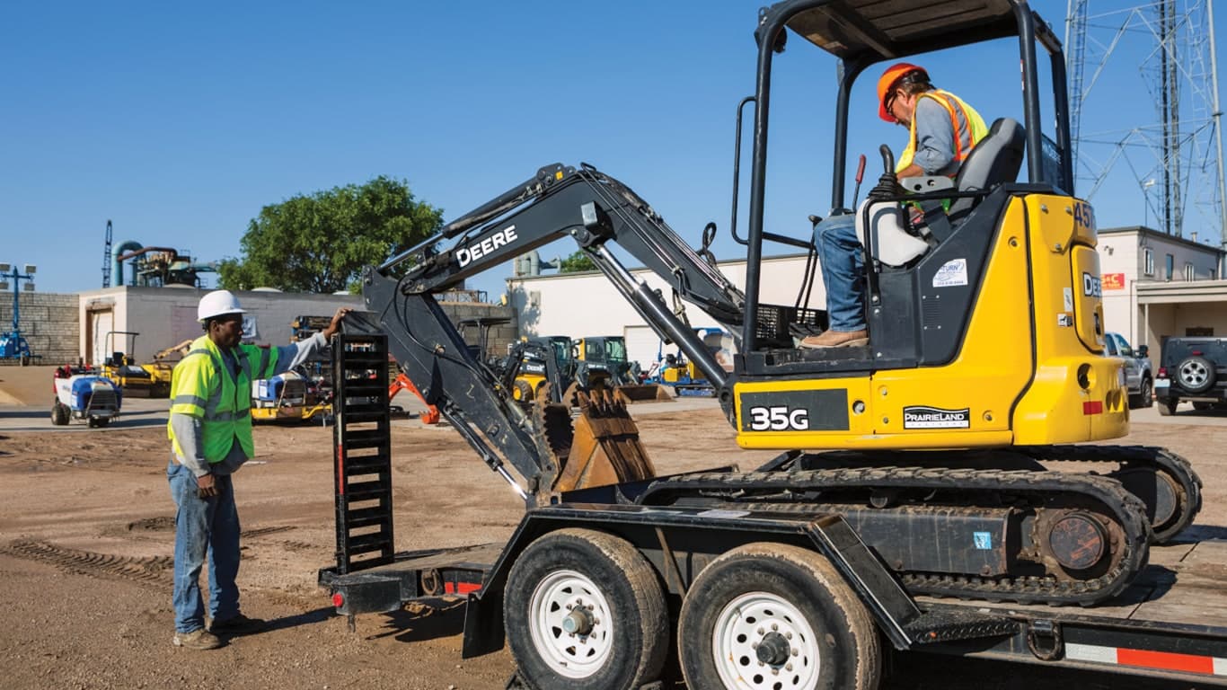 Two operators loading a 35G Excavator onto a flatbed trailer at a worksite. | 4re Equipment | ID: 035gxff