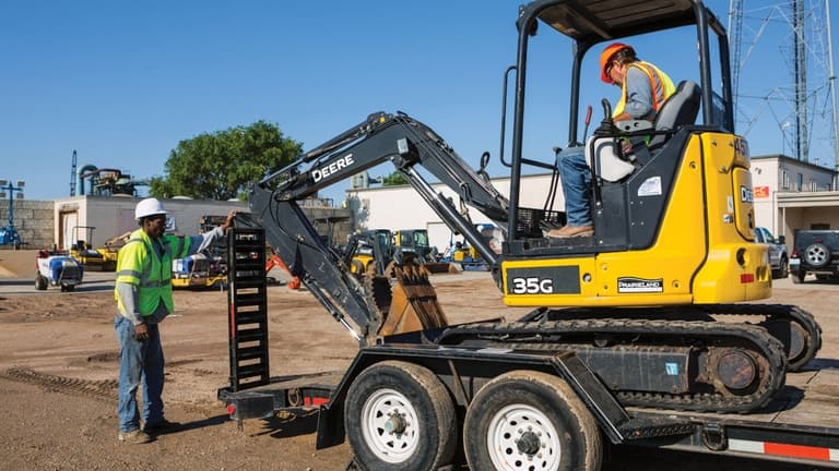 Two operators loading a 35G Excavator onto a flatbed trailer at a worksite. | 4re Equipment