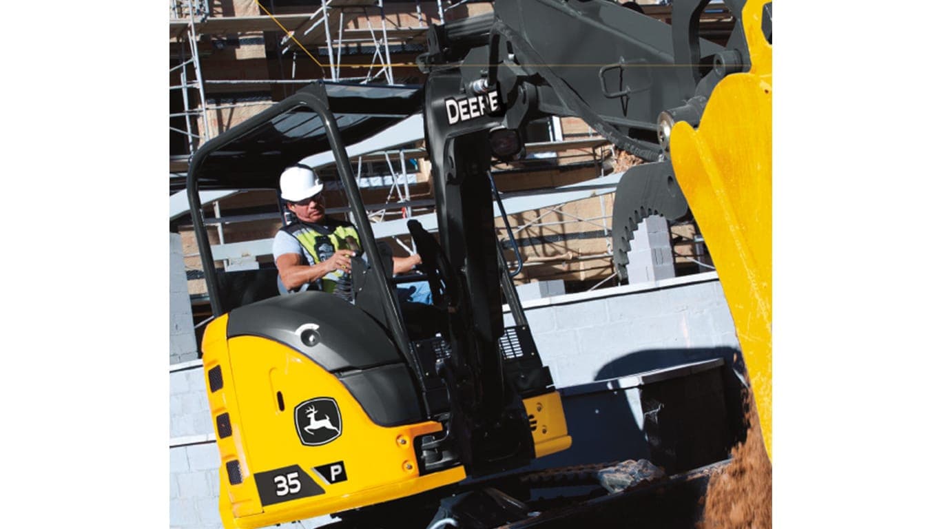 A close-up of an operator using a 35P-Tier Excavator to move dirt at a worksite with building construction in the background. | 4re Equipment | ID: 35PEXFT4