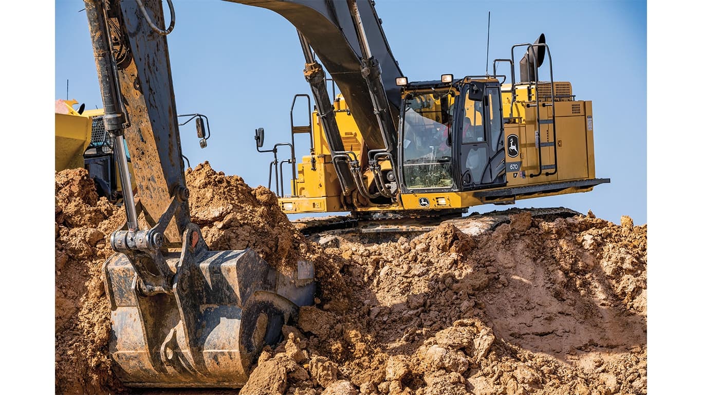 An operator using a 670P-Tier Excavator to scoop up dirt at a worksite with an articulated dump truck to the left. | 4re Equipment | ID: 670PEXFT4