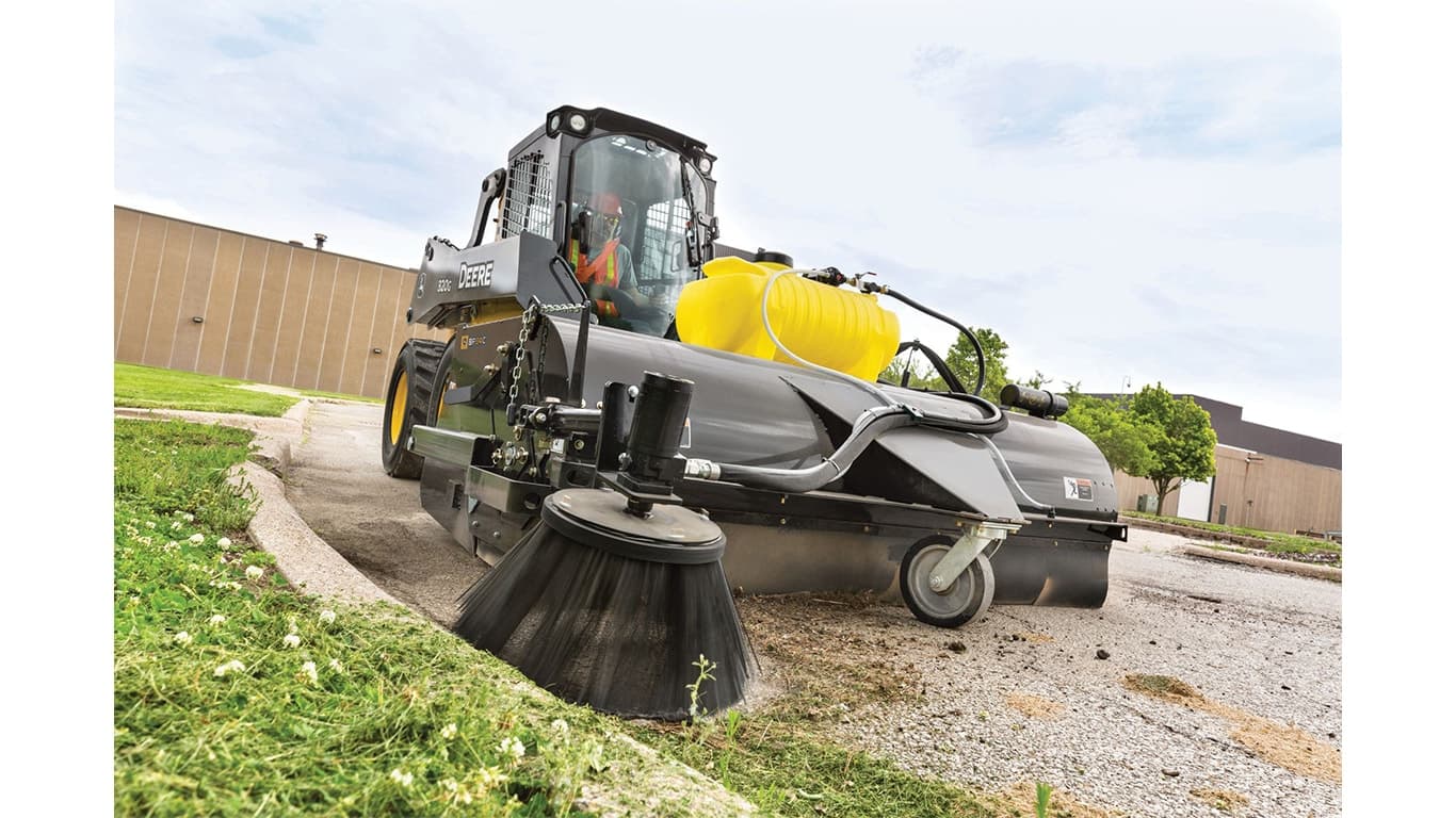 A 320G Skid Steer with a pick-up broom attachment sweeps grass clippings off the road and gutter. | 4re Equipment | ID: 320gxt