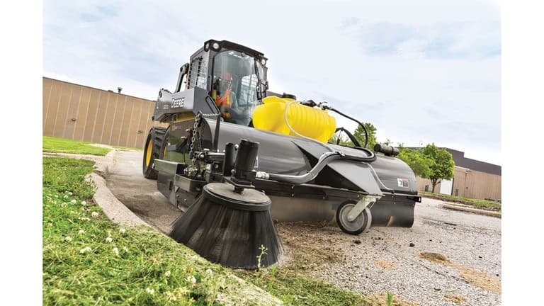 A 320G Skid Steer with a pick-up broom attachment sweeps grass clippings off the road and gutter. | 4re Equipment
