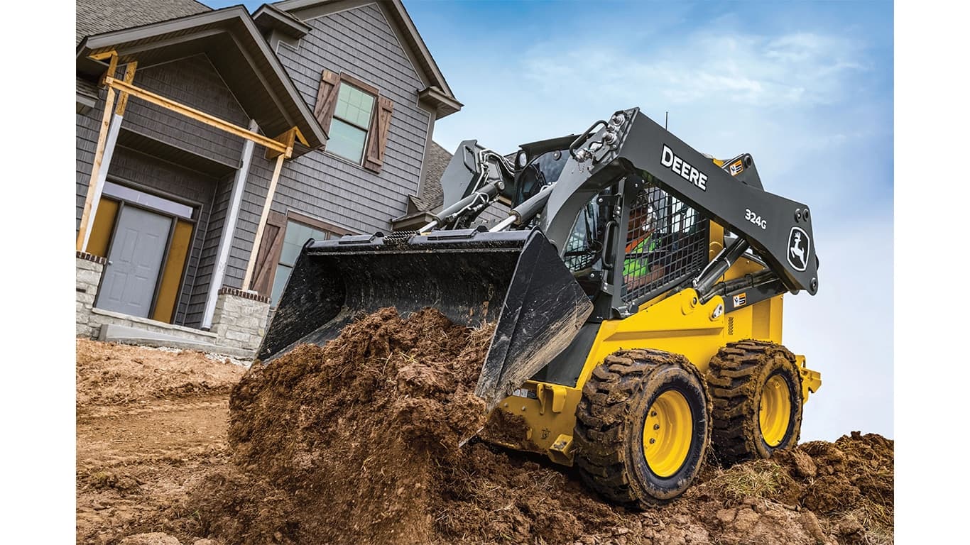 A 324G Skid Steer dumps dirt at a worksite in front of a house. | 4re Equipment | ID: 324gxt